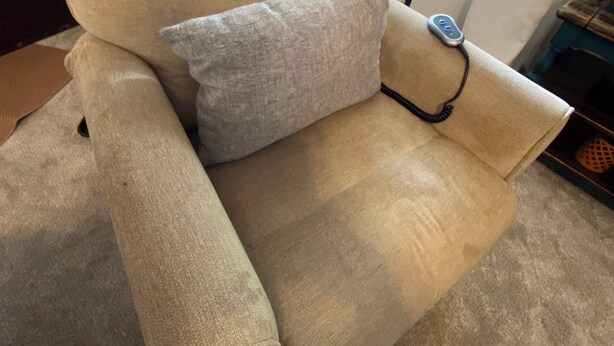 Un fauteuil beige, accompagné d’un coussin assorti et d’une télécommande posée sur l’accoudoir.