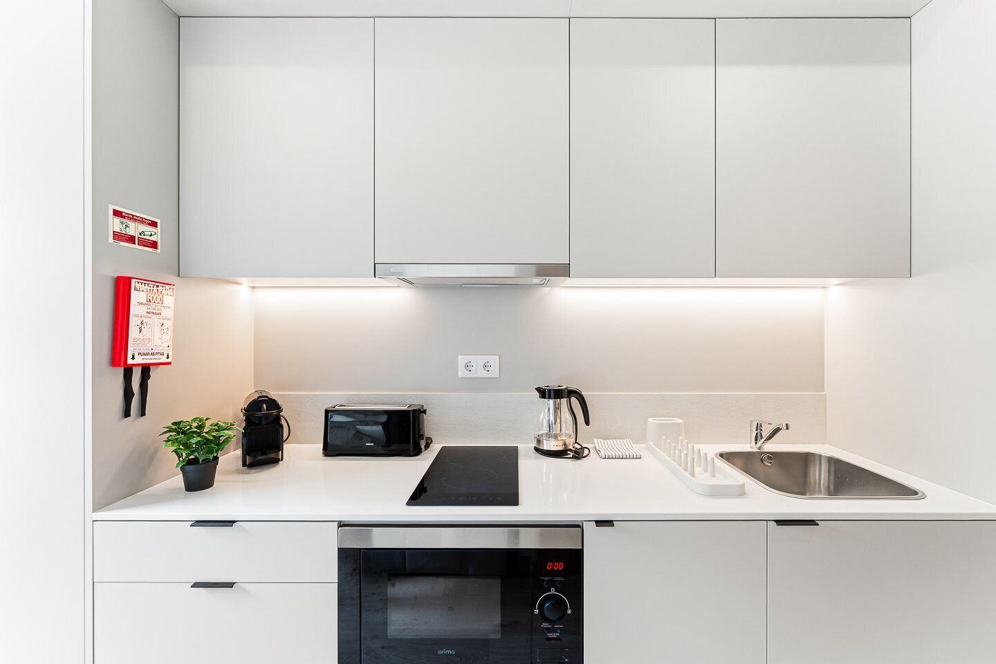 A modern kitchen with white cabinets, a built-in dishwasher, a coffee maker, a toaster, and a sink.