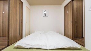 A room with a bed, wooden wardrobe, and a framed picture on the wall. - HANASTAY UMI (Osaka)