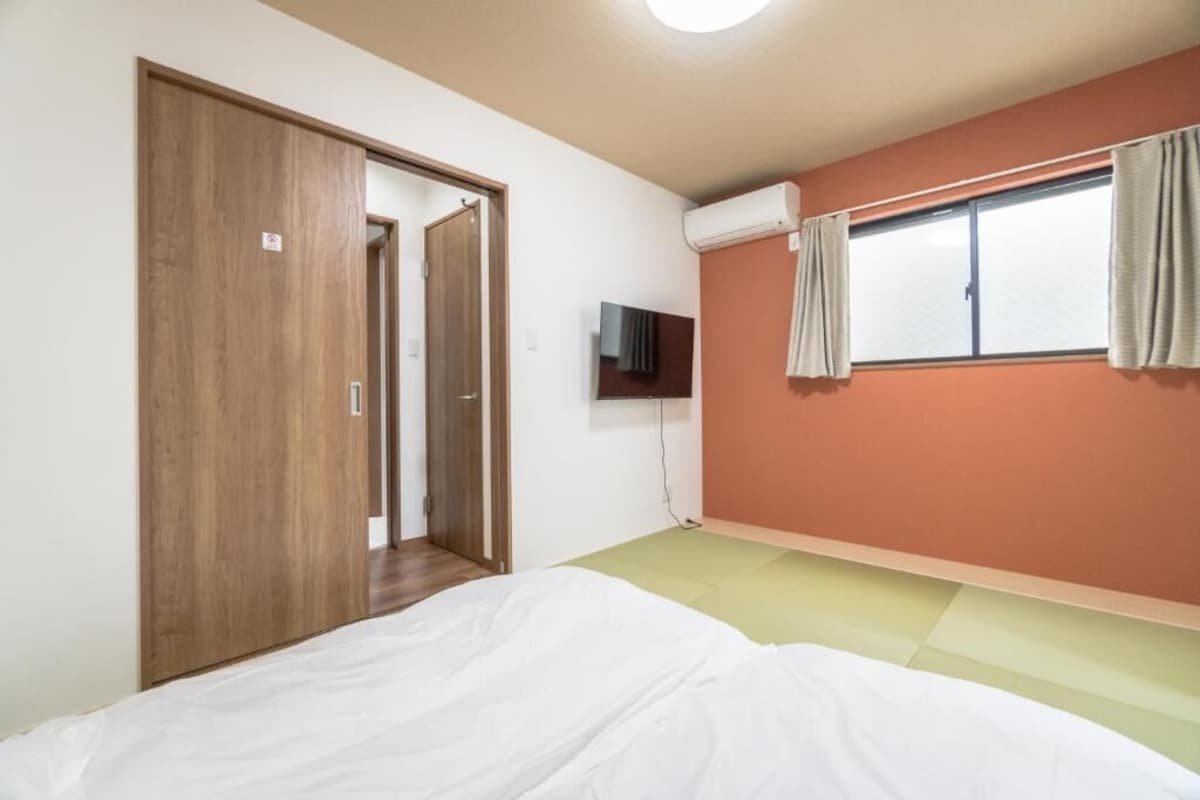 A bedroom with a bed, a television, a window with curtains, and a door.