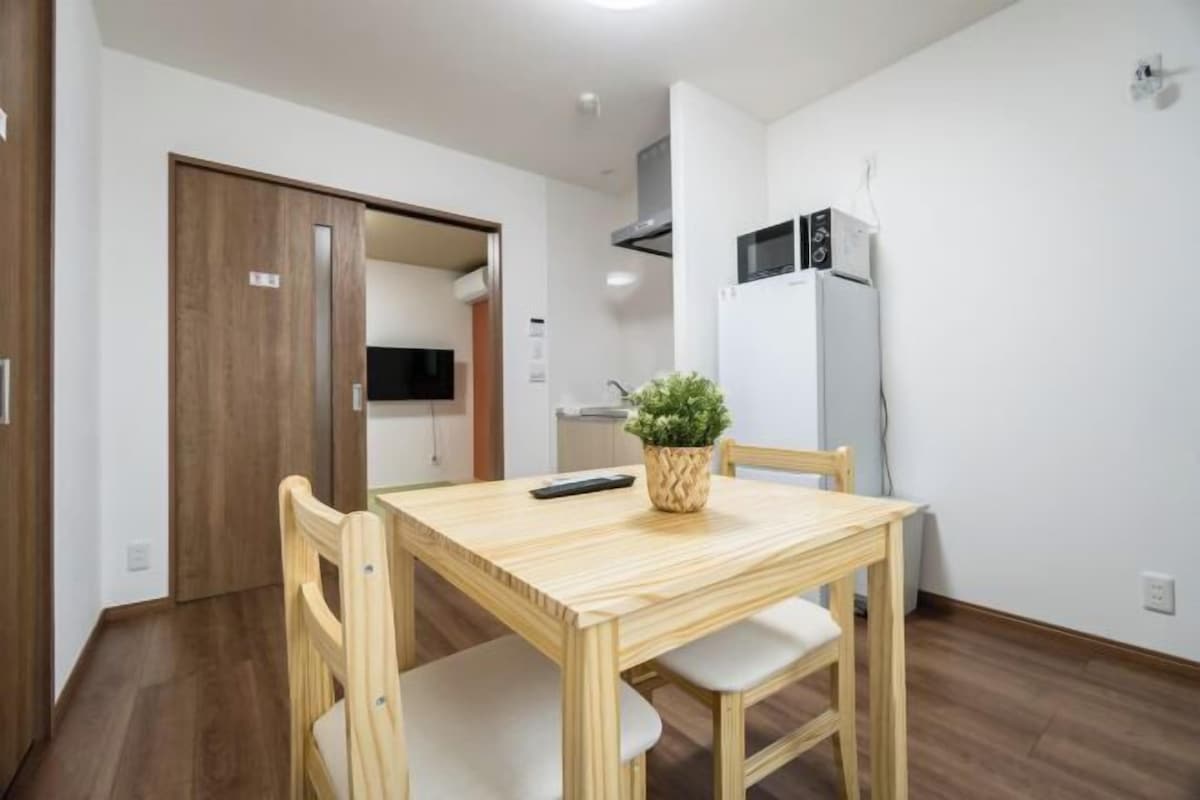 A small kitchen with a microwave, refrigerator, and a wooden table with two chairs.