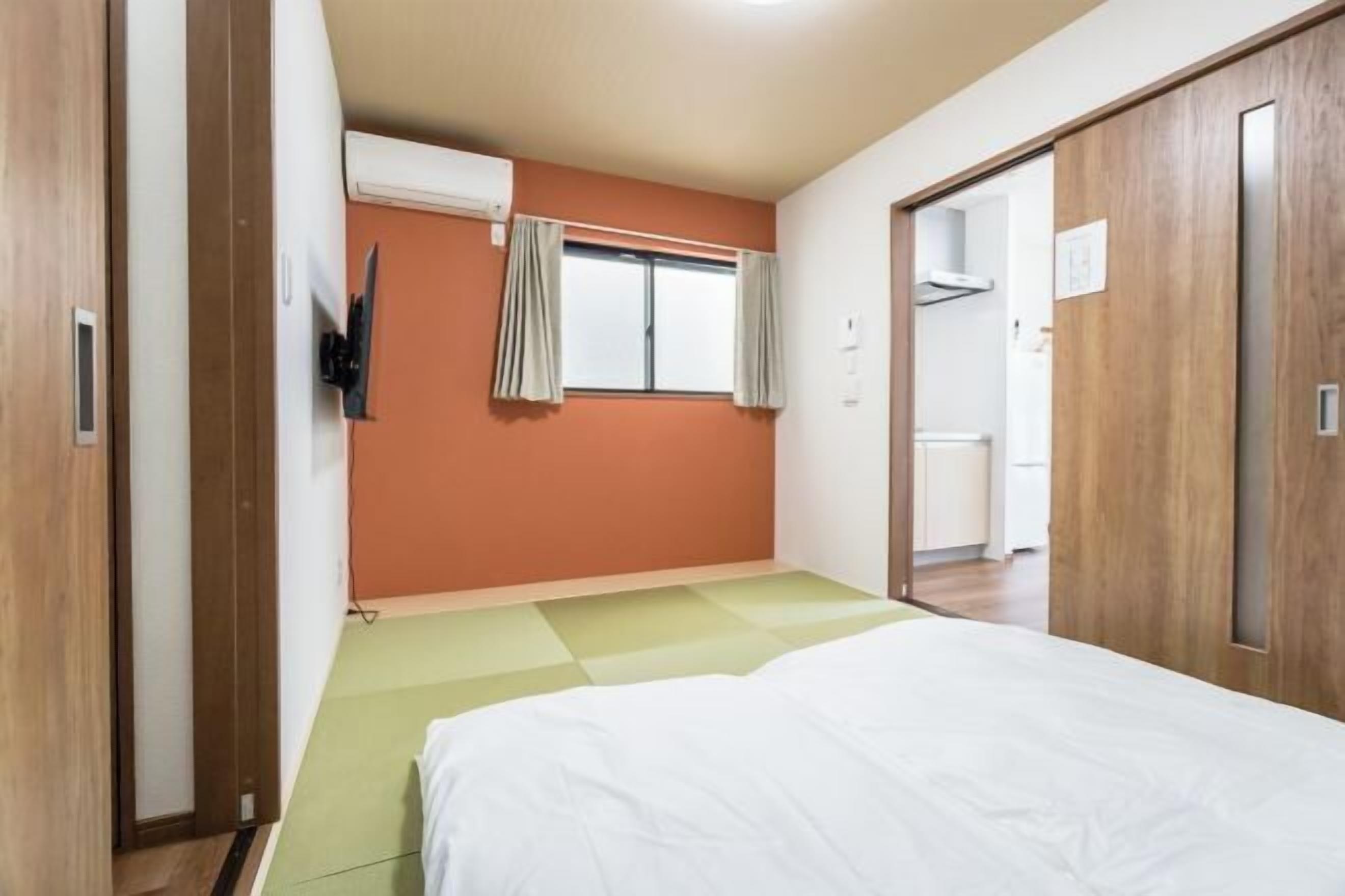 A bedroom with a bed, a window with curtains, an air conditioning unit, and a wooden wardrobe.