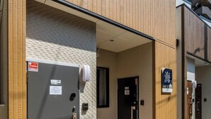 A hotel entrance with a grey utility box, a black door, and a sign with Japanese characters. - HANASTAY UMI (Osaka)