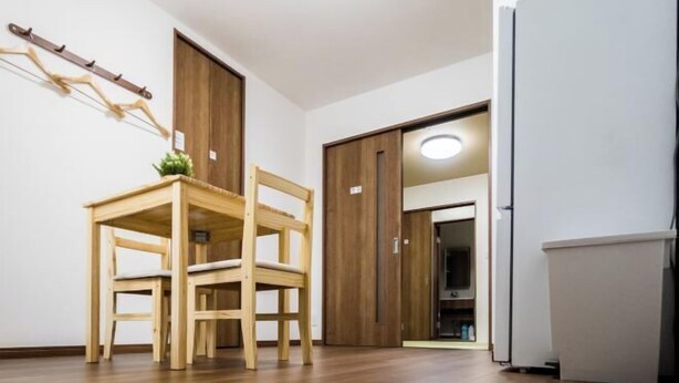 A room with a wooden dining table and chairs, a white refrigerator, and a wooden wardrobe. - HANASTAY UMI (Osaka)