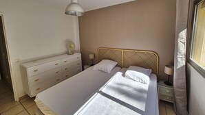 Et soveværelse med seng, kommode, natbord, lampe og loftventilator.