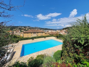 A swimming pool with a tiled deck, surrounded by greenery and a view of a residential area with houses and hills in the background. - Sea view, 4 sleeps, all on foot (ST MANDRIER SUR MER)