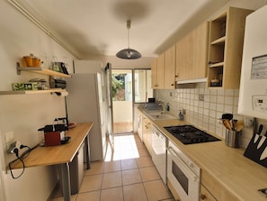 A kitchen with a gas stove, oven, and a sink. There is a window providing natural light, and a door leading to a balcony. - Sea view, 4 sleeps, all on foot (ST MANDRIER SUR MER)