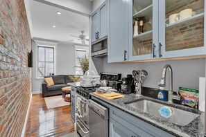 A kitchen with grey cabinets, a black countertop, a stove, and a sink. - NYC Apartment 346-D (New York)
