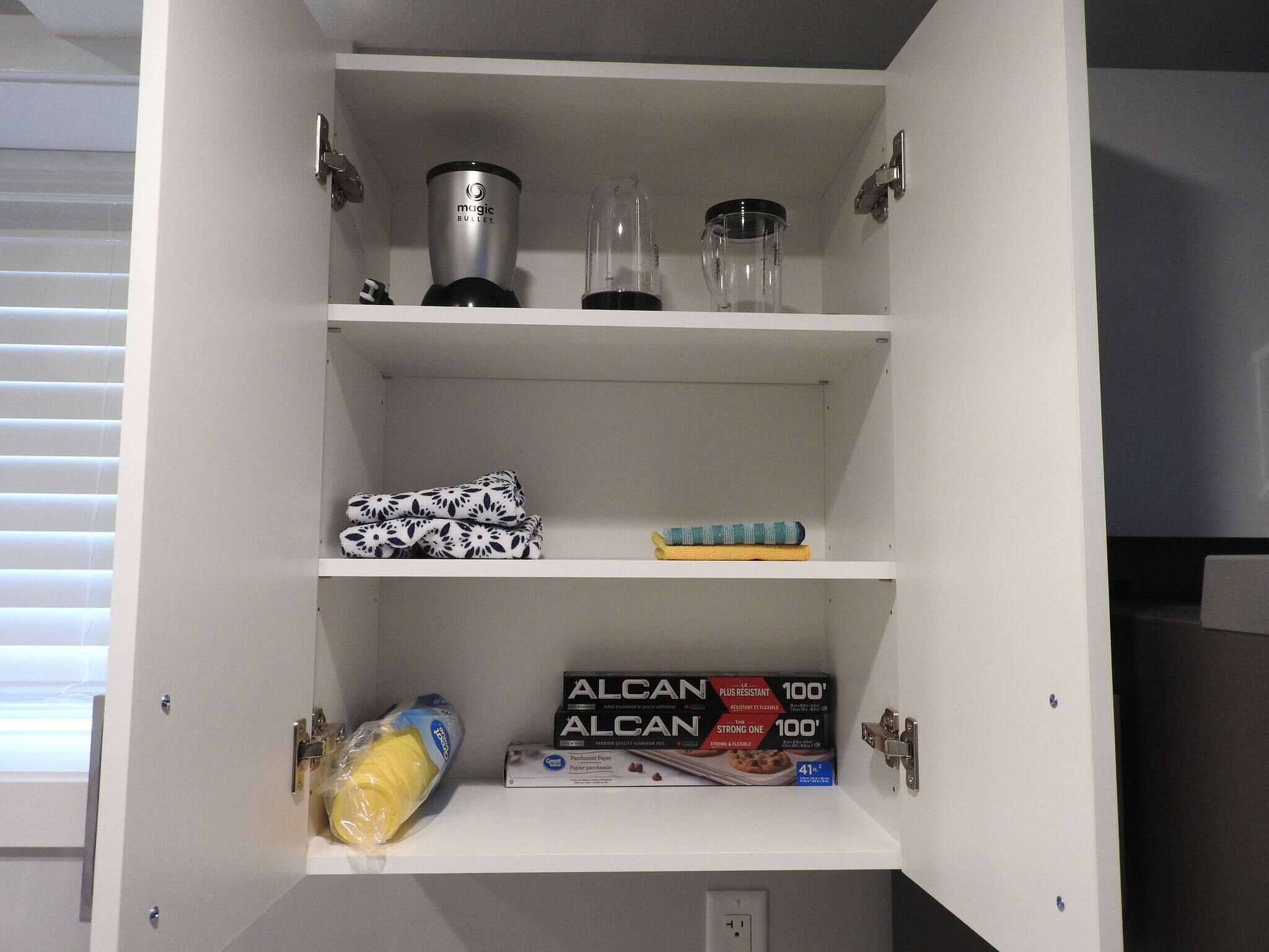 Un mueble de cocina con estantes que contiene electrodomésticos, una toalla enrollada y productos de papel.