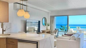 Een moderne keuken met een centraal eiland, een zithoek met een witte bank en een groot raam met uitzicht op de oceaan.
