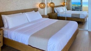Een tweepersoonsbed met houten frame, twee nachtkastjes en een grote spiegel die een balkon en uitzicht op zee weerspiegelt.