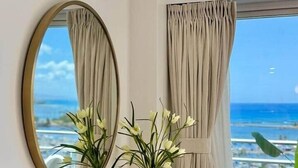 Een kamer met een groot raam, een spiegel, een vaas met bloemen en een houten console tafel.