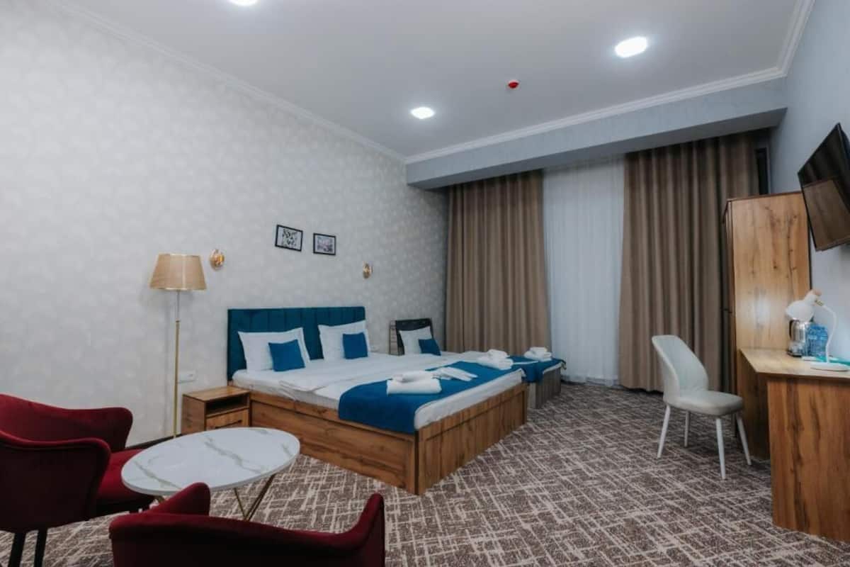A hotel room with a bed, a desk, a chair, a small table, and a TV.