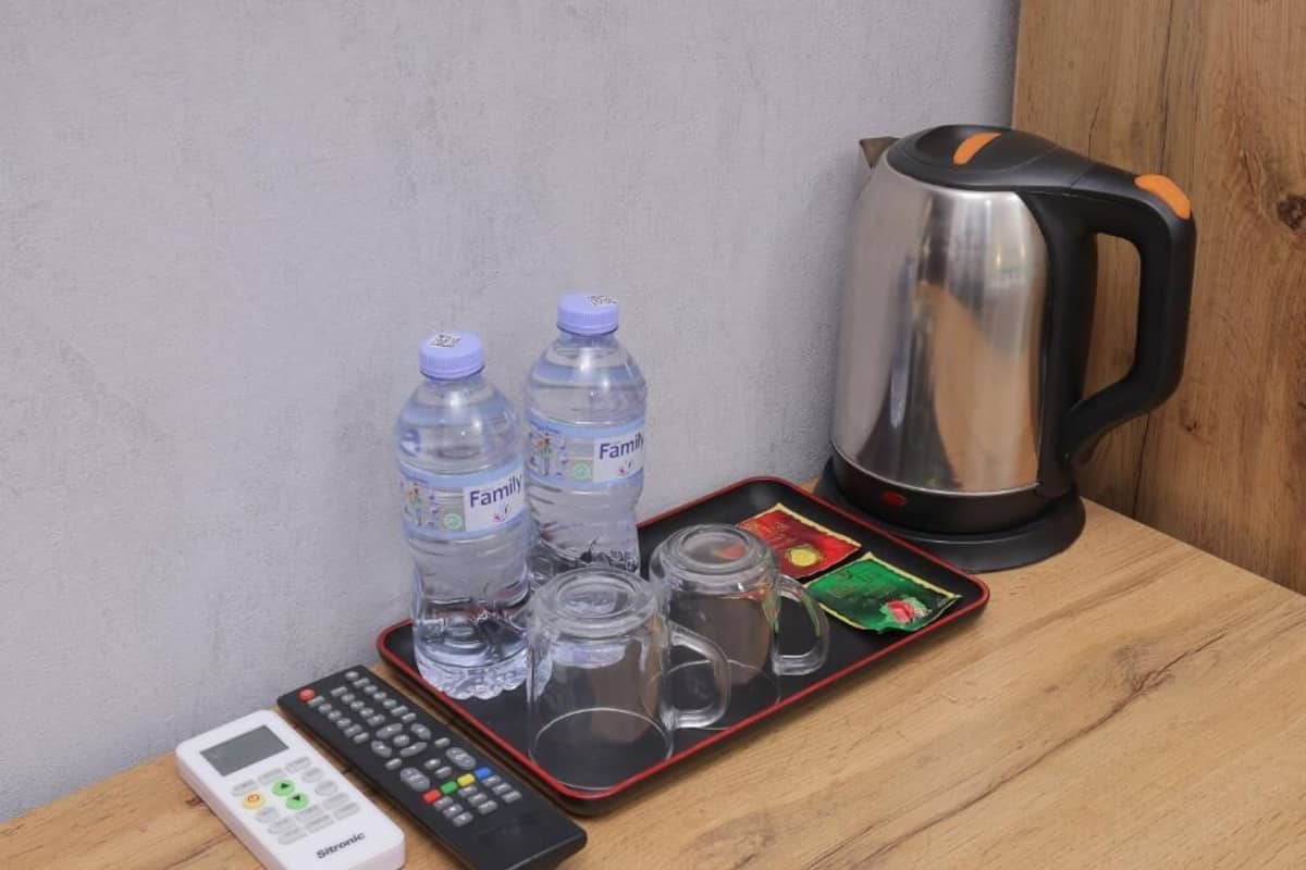 A tray with two water bottles, a kettle, a remote control, and a smartphone on a wooden surface.
