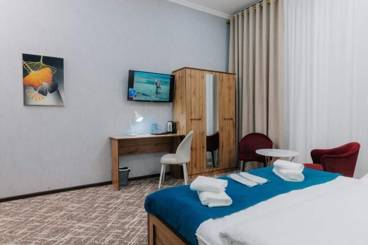 A hotel room with a bed, a desk with a chair, a television, a wardrobe, and a small table with a chair.