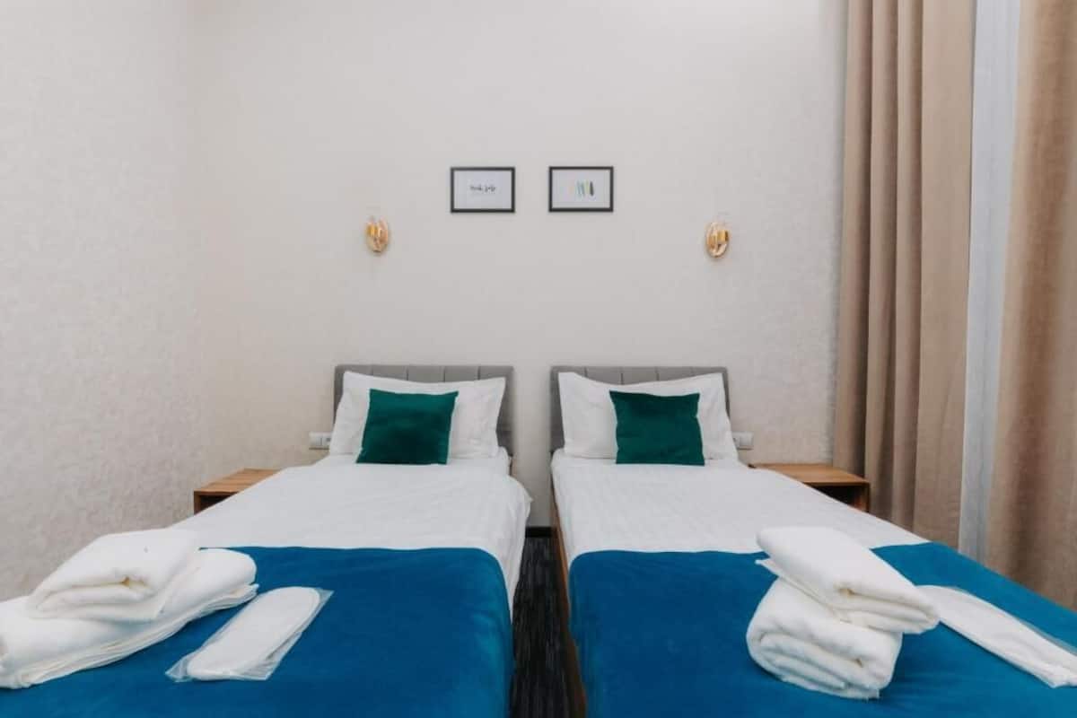 A hotel room with two single beds, white bedding, teal pillows, and a blue accent bedspread.