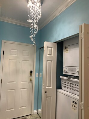 Un couloir avec une porte blanche, une porte blanche avec une poignée, un appareil électroménager blanc doté d’un panneau de commande, et un autre appareil électroménager blanc doté d’un panneau de commande.