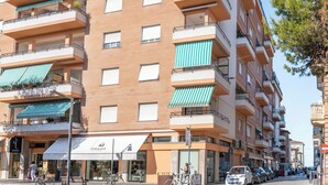 En bygning med flere etager, altaner, en butik med skiltning og parkerede biler.