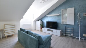 Una sala moderna con techo inclinado, un televisor de pantalla plana, un sofá, un mueble blanco y una planta en maceta.