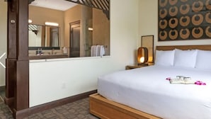 A hotel room with a large bed, a mirror, a wall art piece, a bedside lamp, and a wooden nightstand.