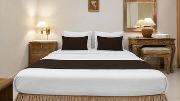 A neatly made bed with a white and black bedspread, two bedside tables with lamps, a wooden nightstand, a mirror, and a small table with a vase.