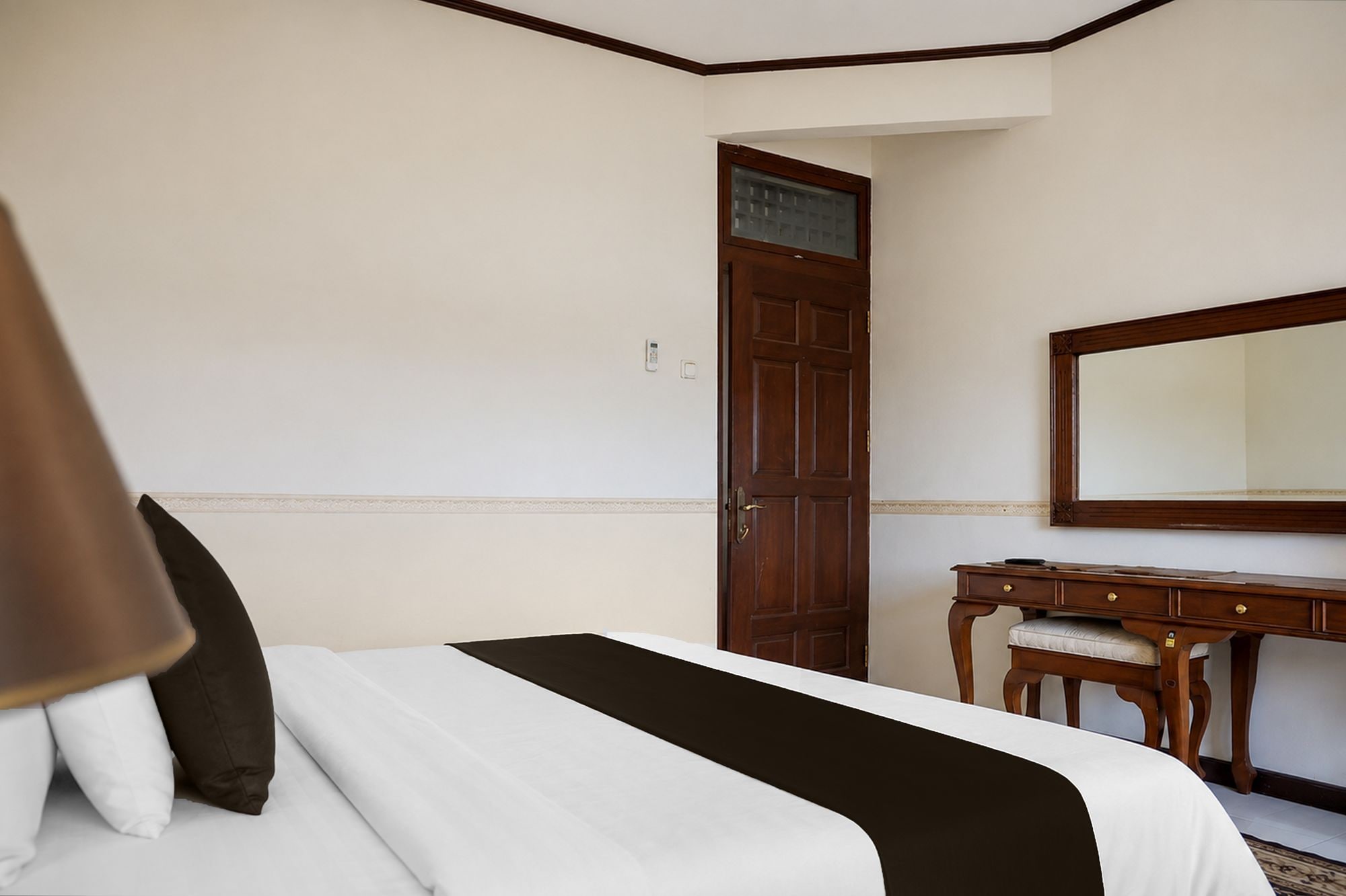Una habitación de hotel con una cama, un aparador de madera, un espejo y una puerta.