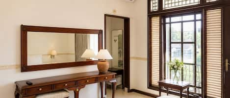Una habitación de hotel con una cama grande, una consola de madera con lámparas, un espejo y una ventana con persianas.