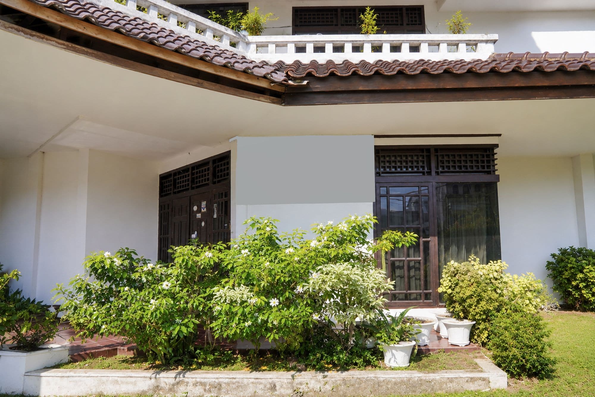 A building with a tiled roof, a balcony, and a large window. There are potted plants and a small garden area.