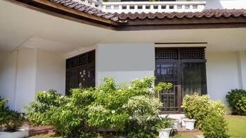 A building with a tiled roof, a balcony, and a large window. There are potted plants and a small garden area.