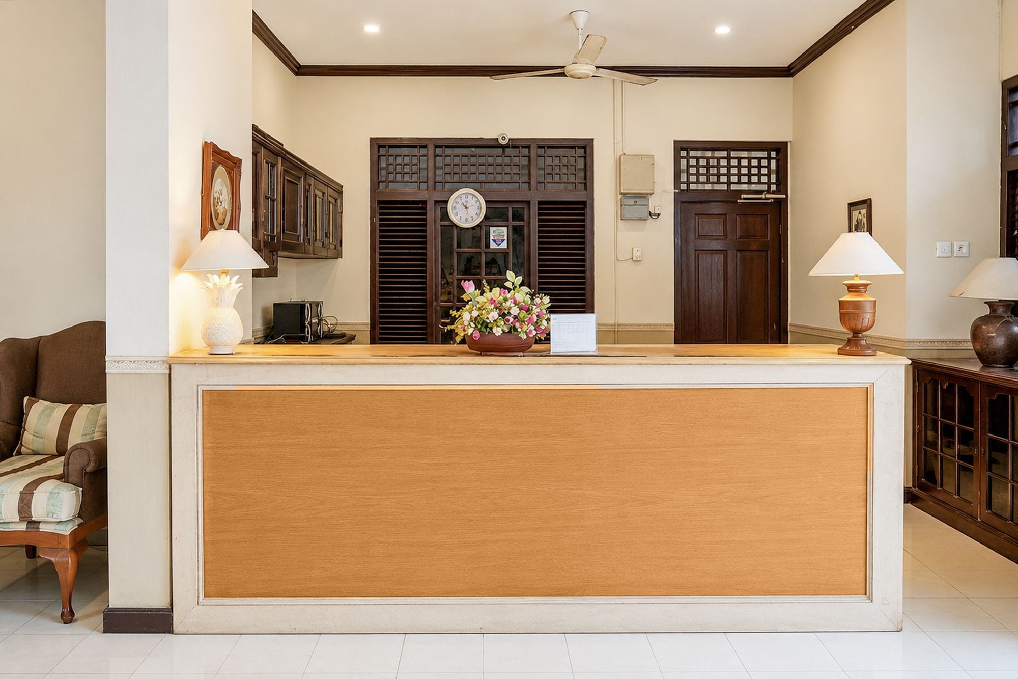 A reception area with a wooden reception desk, a clock, and a flower arrangement.