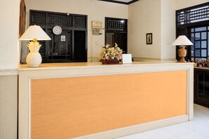A reception desk with a wooden panel, two wall-mounted clocks, a potted plant, and a calendar. - Hotel O near Pantai Padang formerly Bou (Padang)