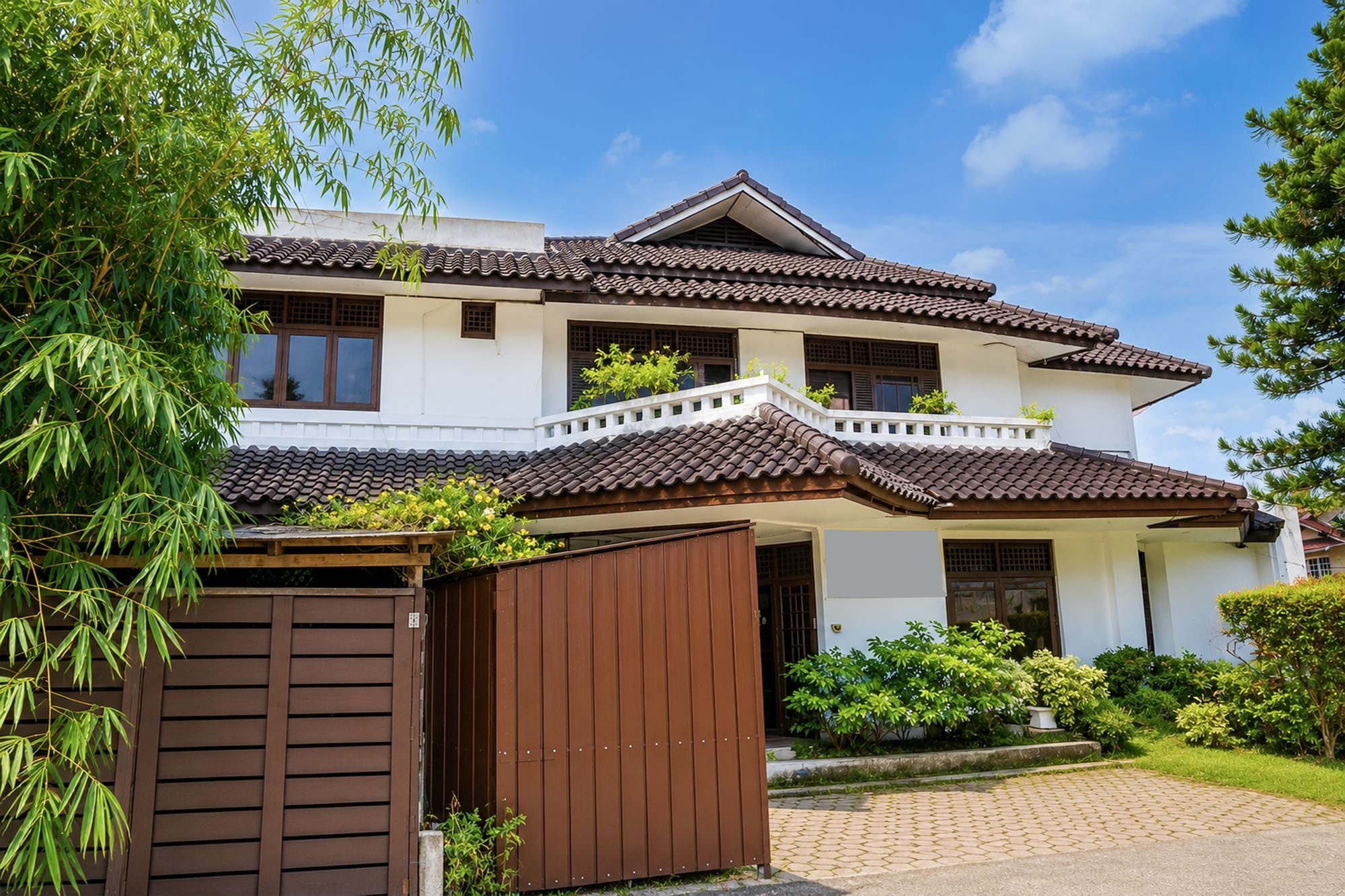 A two-story house with a tiled roof, a wooden gate, and a well-maintained garden.