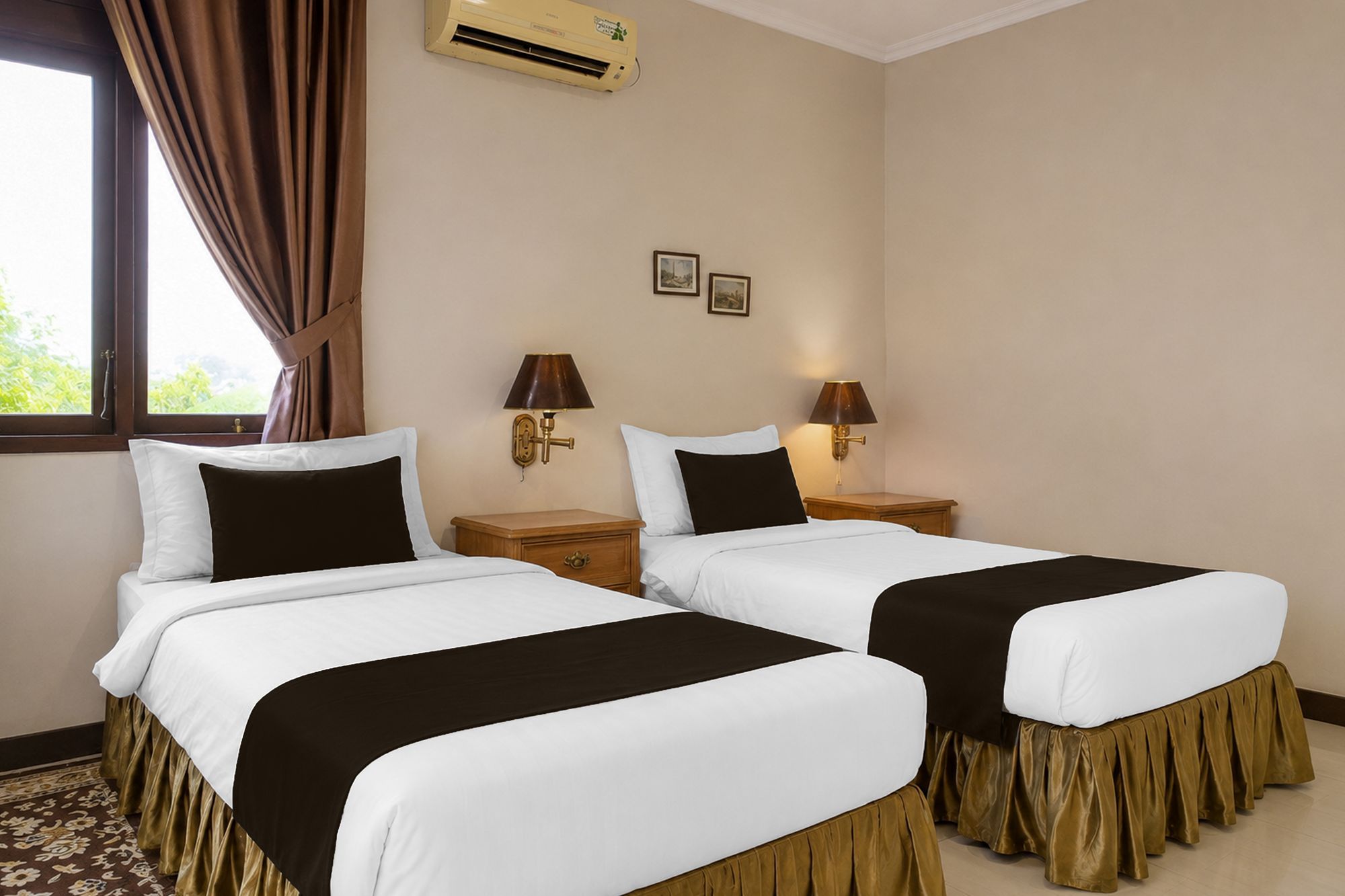 A hotel room with two beds, a window with curtains, an air conditioning unit, and two wall-mounted lamps.