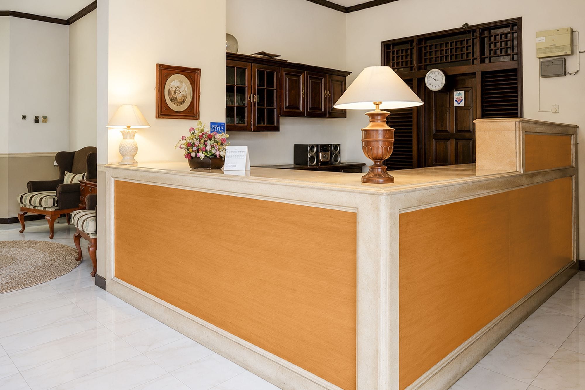 A reception desk with two lamps, a clock, and a calendar on the wall.