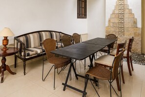 A dining area with a striped sofa, wicker chairs, a dark wooden table, and a lamp. - Hotel O near Pantai Padang formerly Bou (Padang)