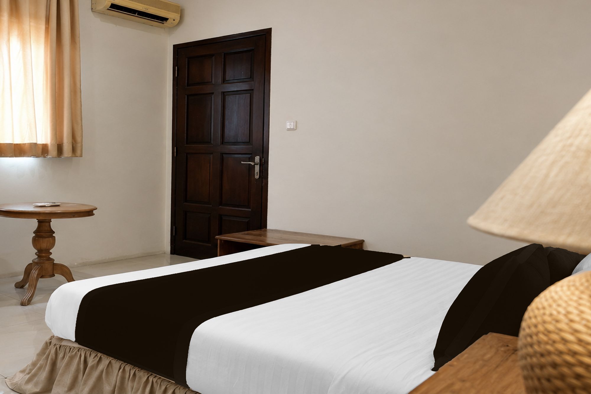 Una habitación con cama, una mesita, una puerta y una lámpara.
