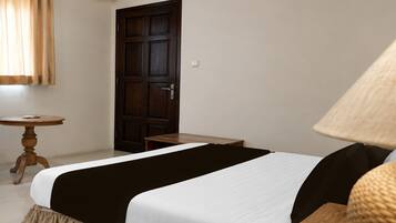 Una habitación con cama, una mesita, una puerta y una lámpara.