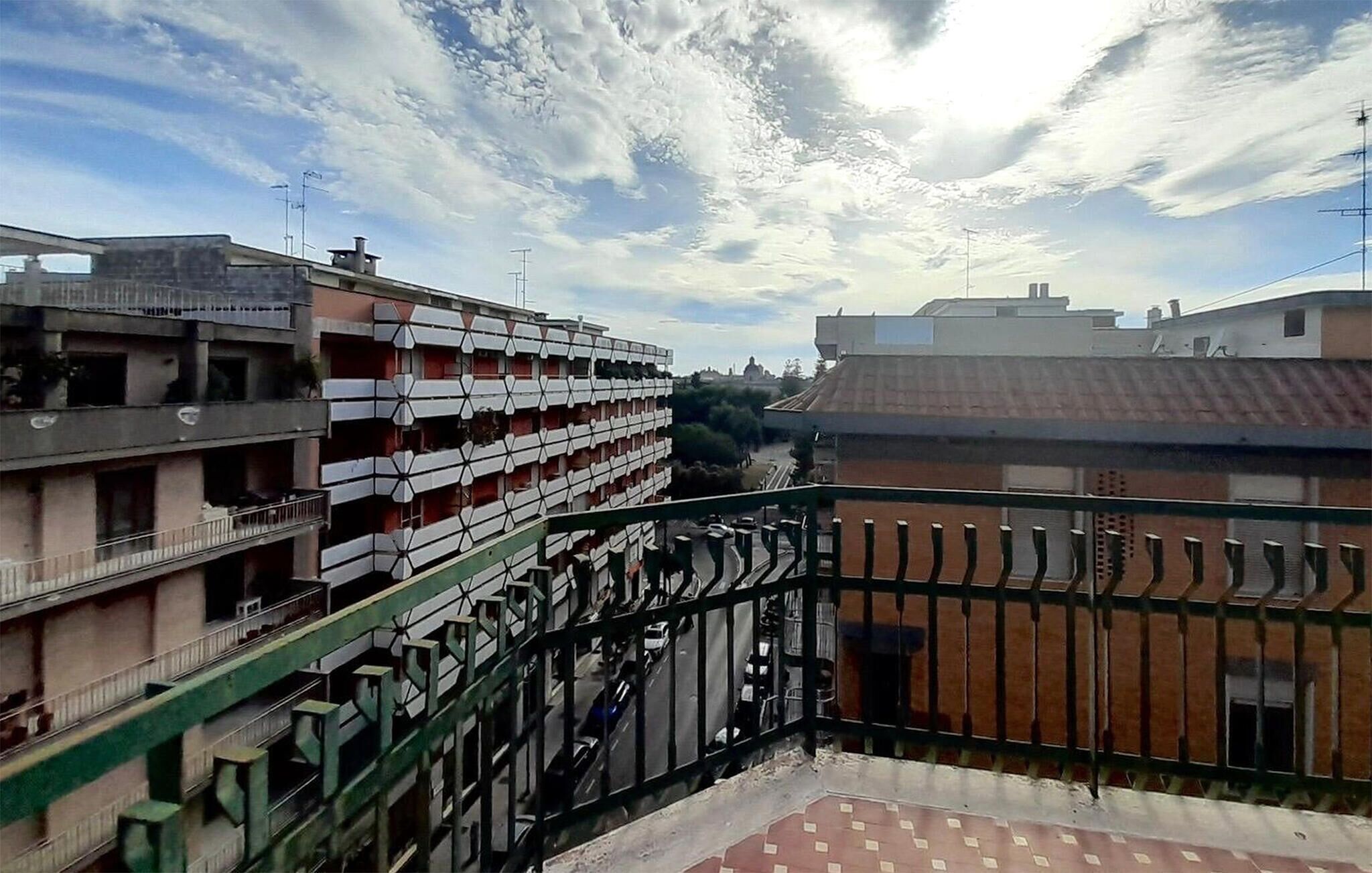 A multi-story building with balconies, a green metal railing, and a clear sky with clouds.