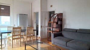 Een moderne woonkamer met een grijze bank, een houten eettafel met stoelen, een glazen salontafel en een ingebouwde houten boekenkast.