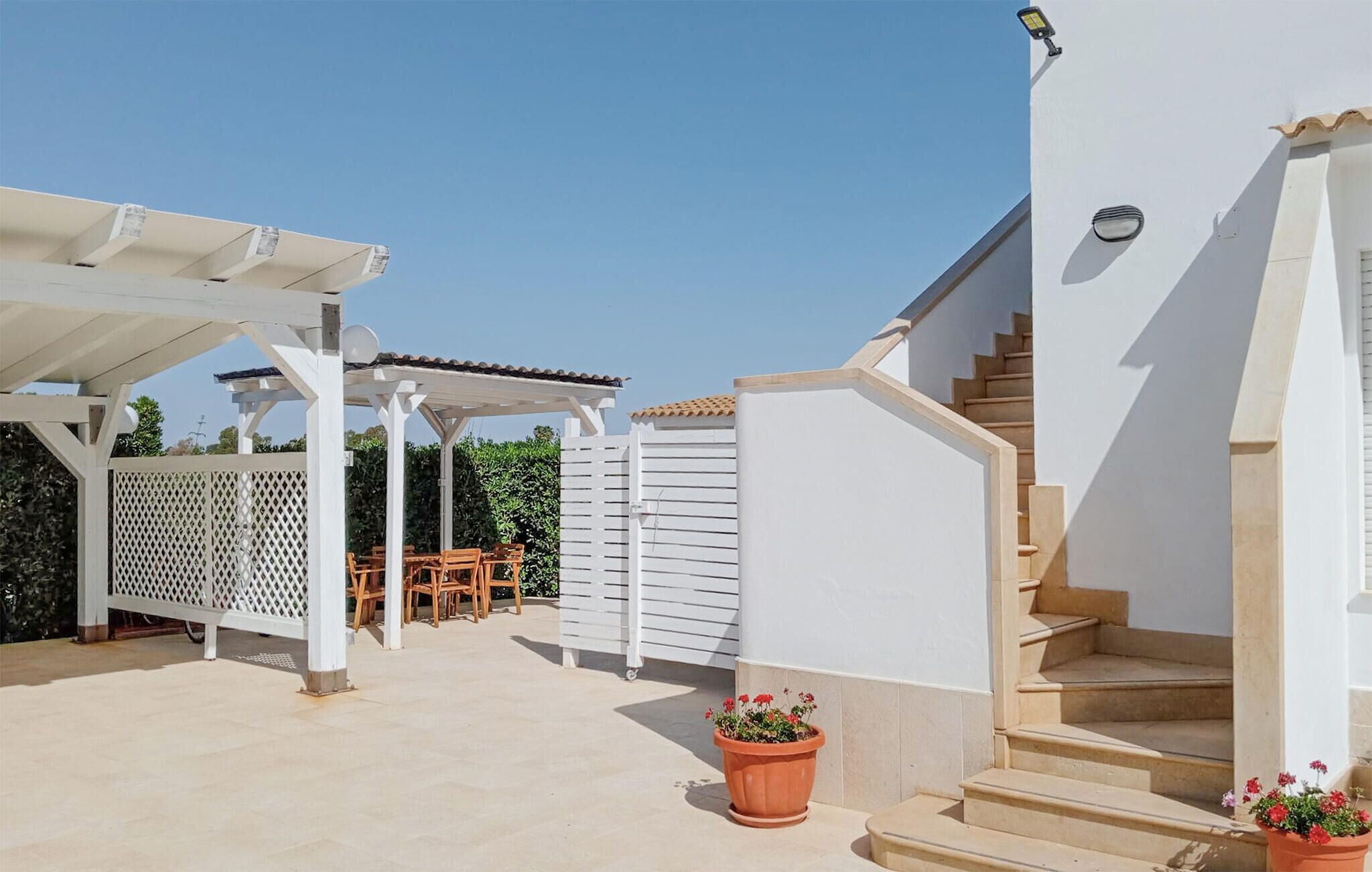Une terrasse couverte avec des meubles d’extérieur, un bâtiment blanc avec un escalier et une caméra de surveillance.