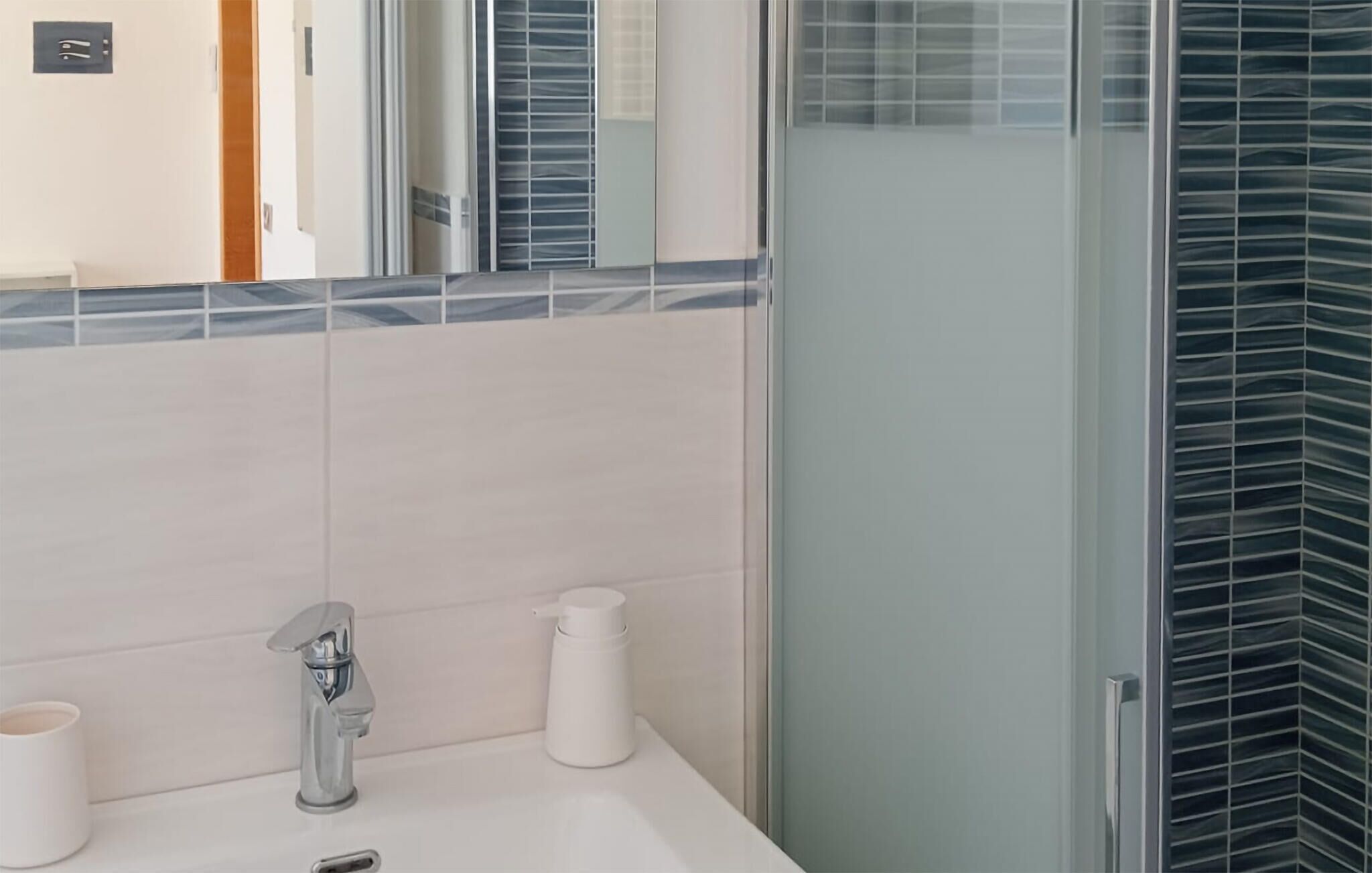 Un baño moderno con un lavamanos blanco, un grifo cromado, un espejo y una ducha con puerta de cristal.