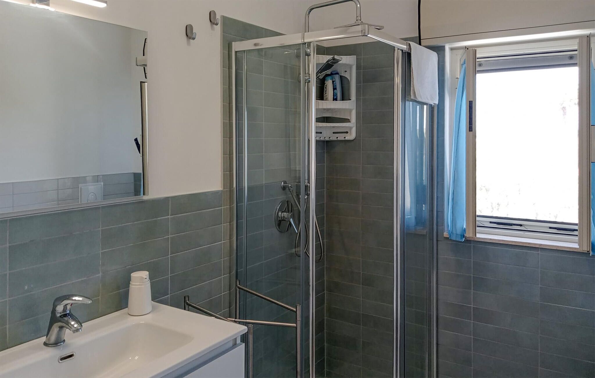 Un baño con ducha acristalada, lavabo y espejo.