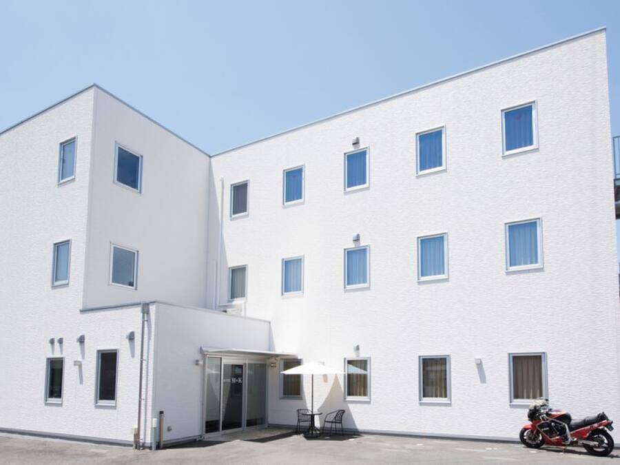 A white multi-story building with a flat facade, several windows, a glass door entrance, and a motorcycle parked outside.