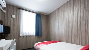 Una habitación de hotel con cama, escritorio, silla, televisor y ventana con cortinas.