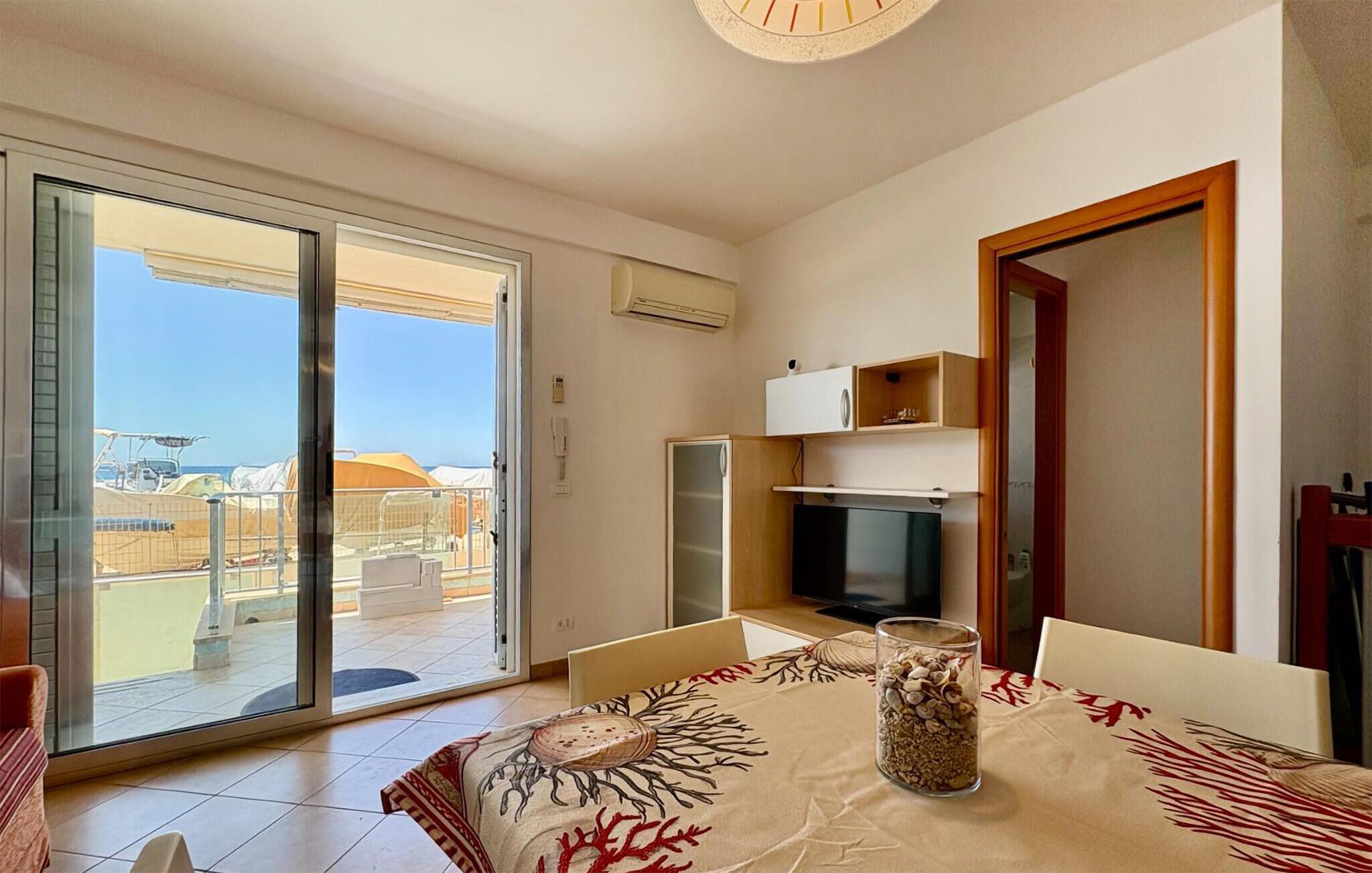 A room with a sliding glass door leading to a balcony, a television, a small cabinet, and a table with a decorative centerpiece.