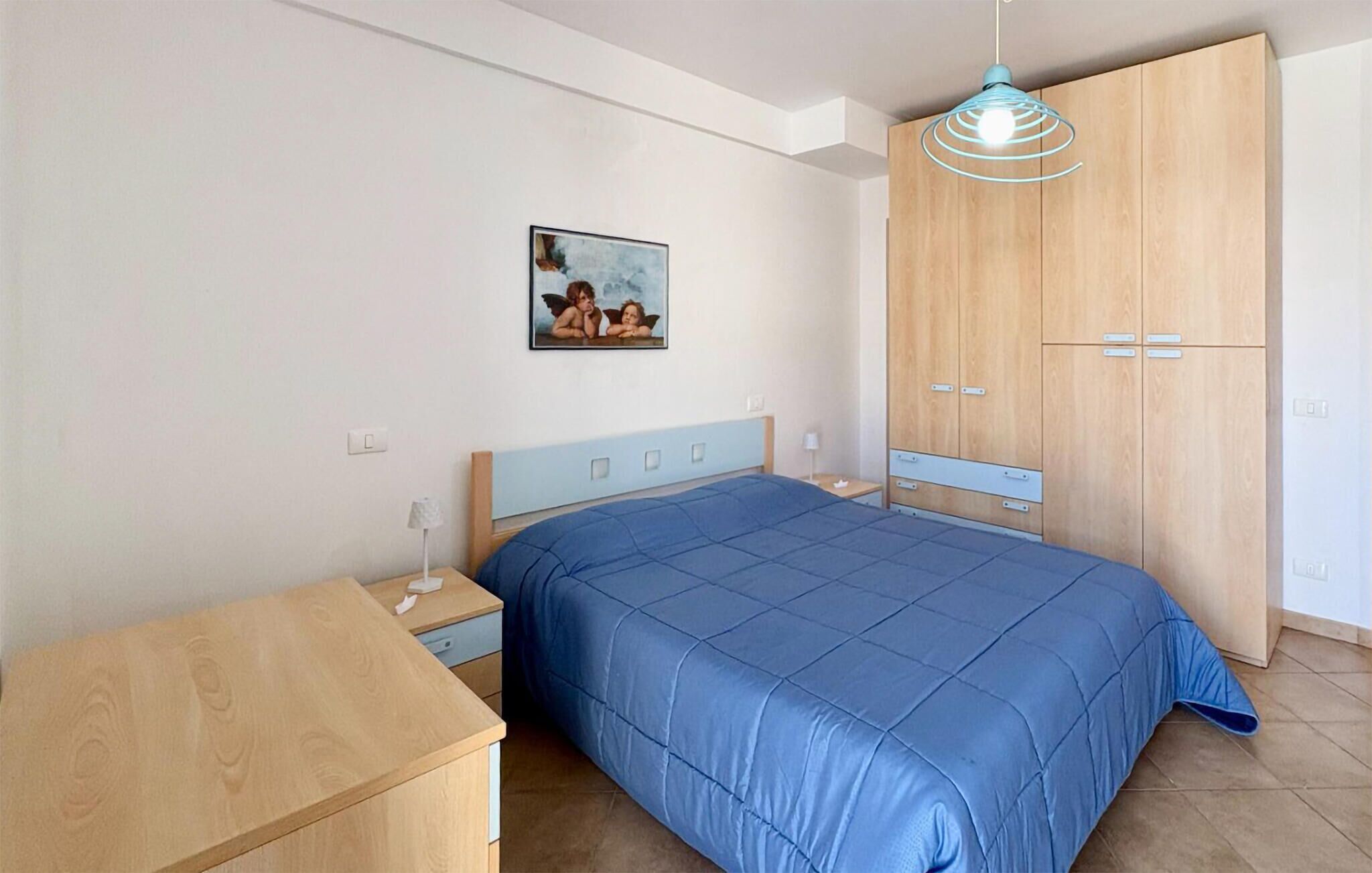 Une chambre à coucher comprenant un lit, une table de chevet, une armoire en bois et un luminaire suspendu.