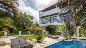 A modern two-story house with a swimming pool, outdoor seating, and lush greenery.