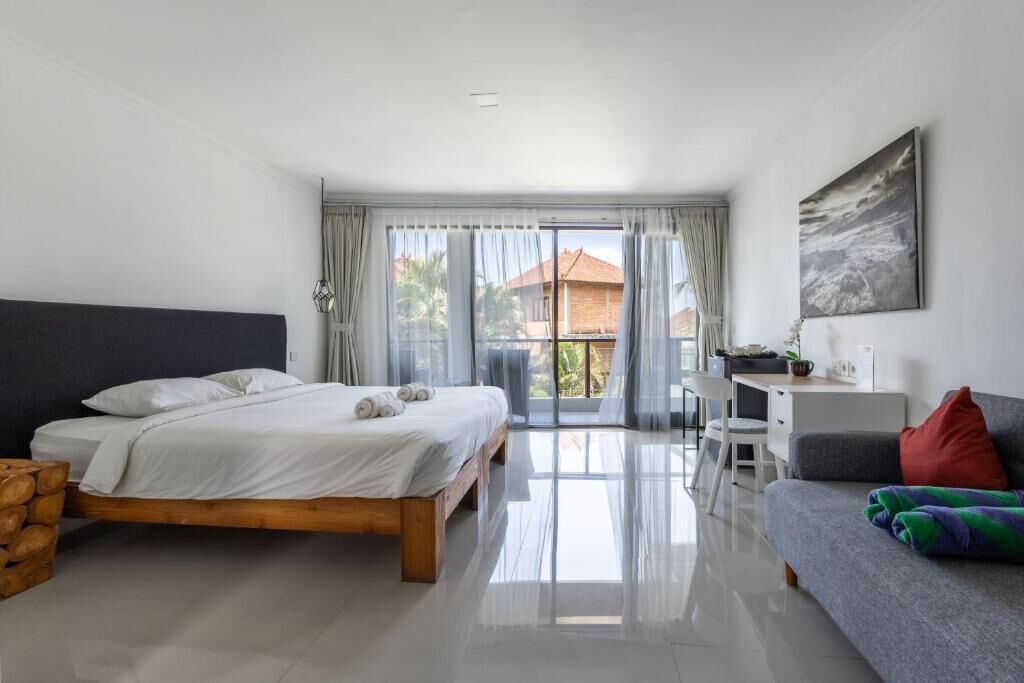A bedroom with a bed, a desk, a sofa, and a balcony with curtains.
