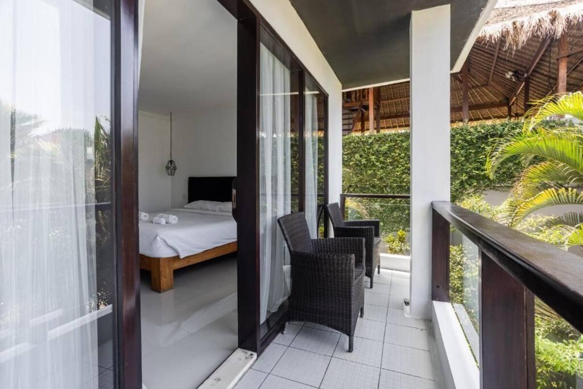 A balcony with a bed, wicker chairs, and a view of greenery.
