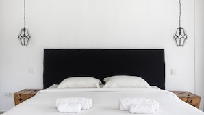 A neatly made bed with white linens and pillows, two bedside tables, and two hanging light fixtures.